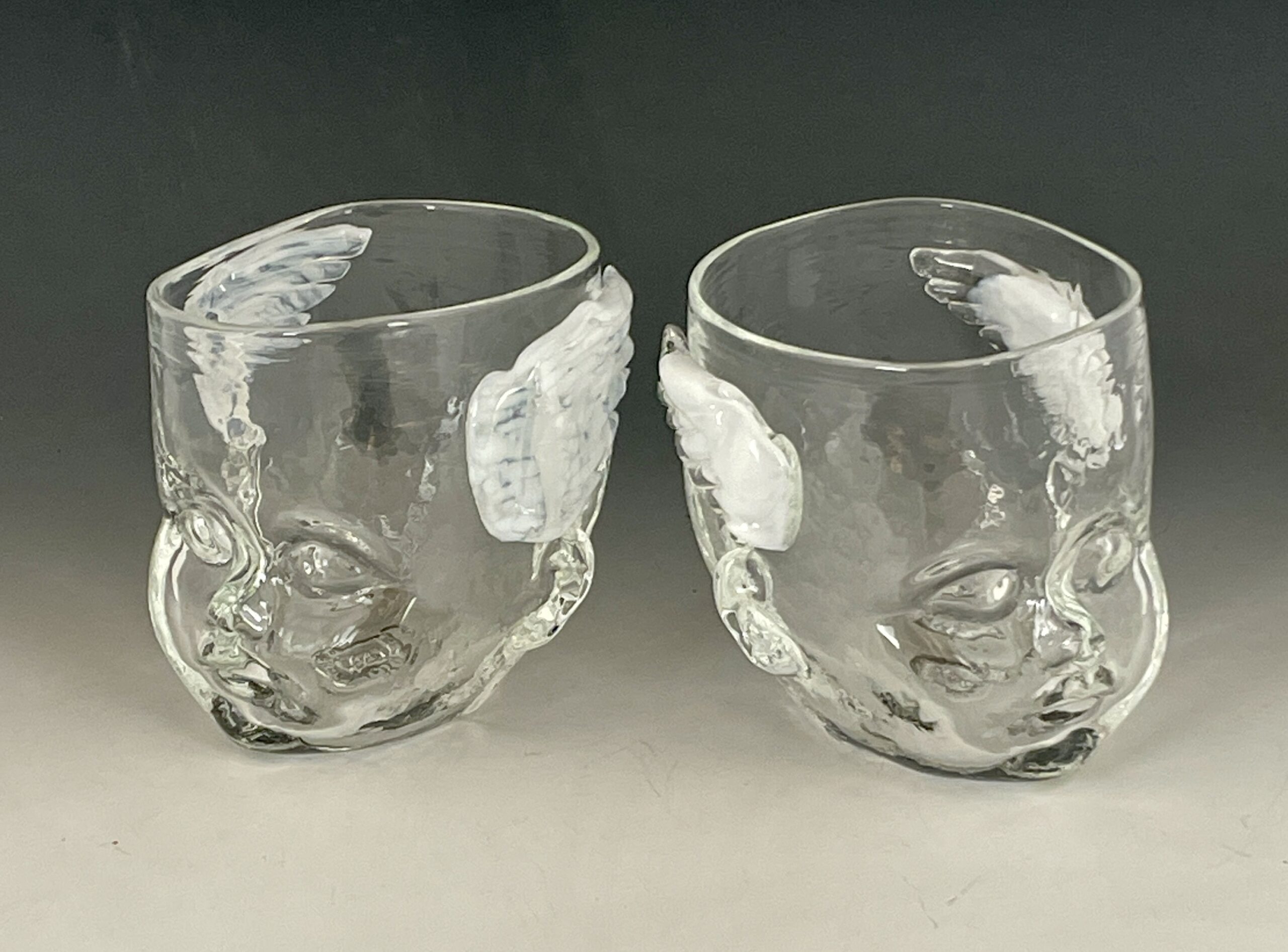 Two white winged Cherub Baby Head Cups facing away from each other.