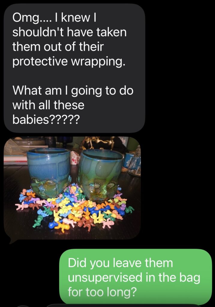A text screenshot with a photo of two dark green baby had cups amongst a pile of multicolored small plastic babies.