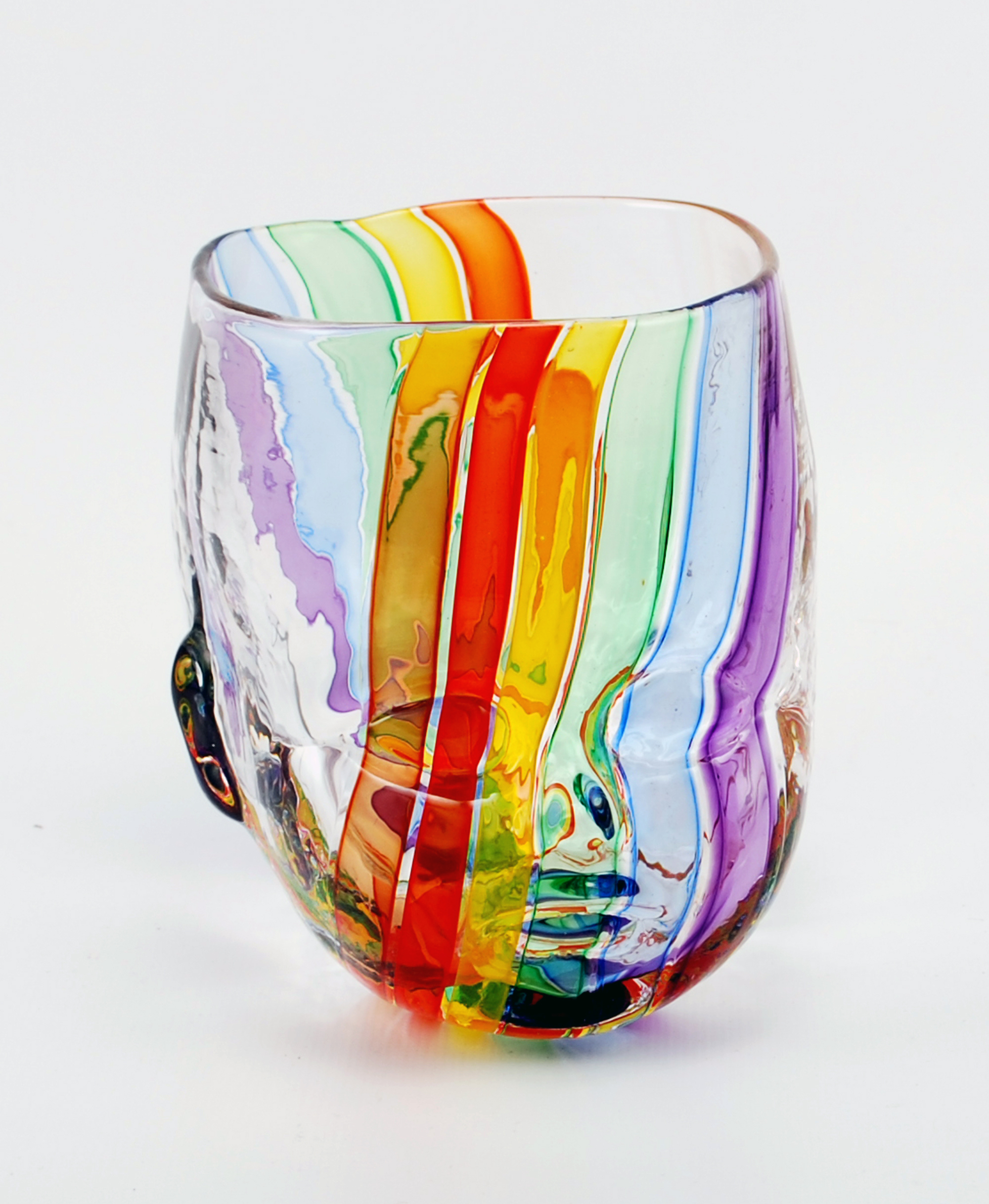 One clear glass in the shape of a dolls head with rainbow stripes in front of a white background.